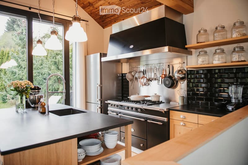 Modern kitchen with stainless steel appliances, wooden cabinets, and a black countertop. Features include a large island with a sink, pendant lights, and various kitchen utensils and appliances.