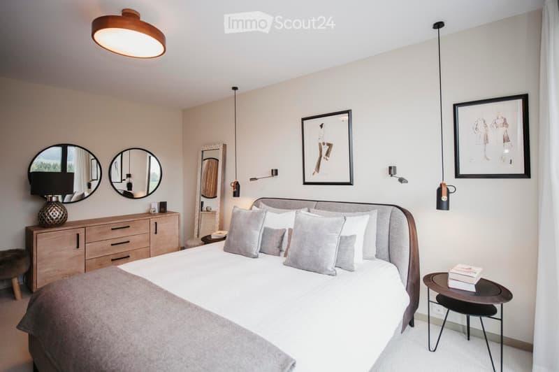 Modern bedroom with a large bed, nightstand, round mirrors, wall-mounted lamps, and decorative artwork.