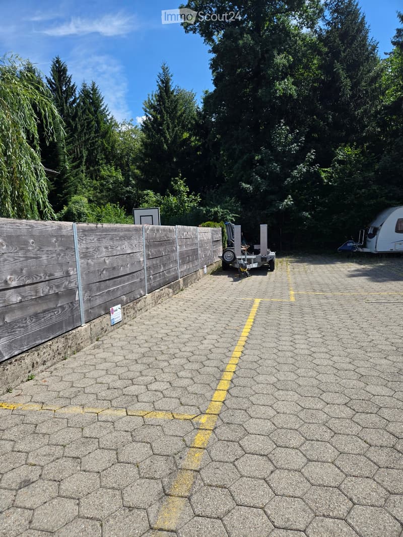 A paved outdoor area with hexagonal stone tiles, a wooden fence on the left, and a trailer and camper in the background.