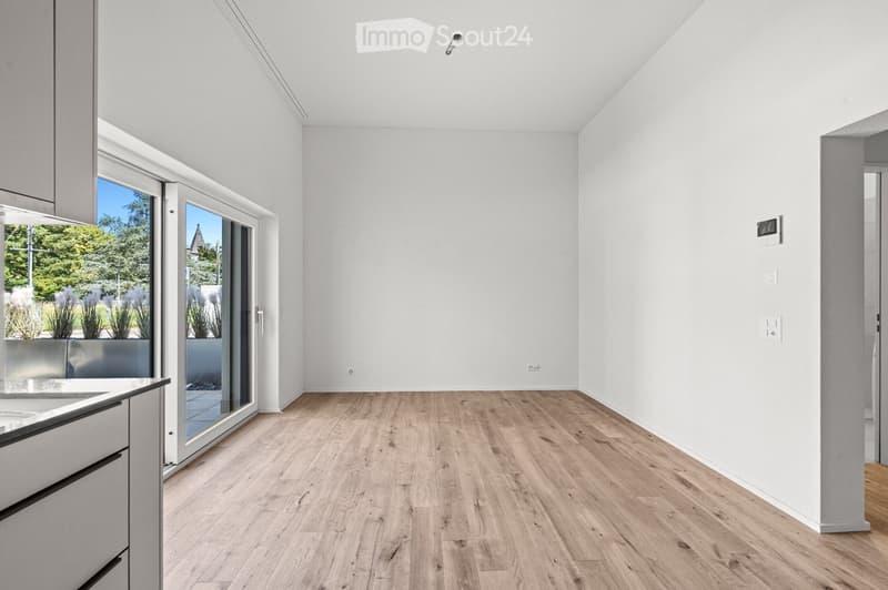 Bright, empty room with light wooden flooring, white walls, and large glass sliding doors leading to an outdoor area.