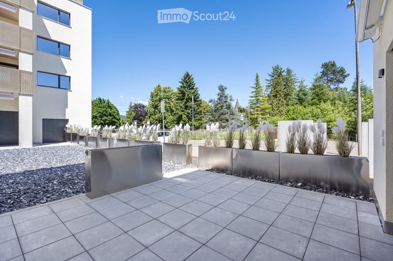 Modern outdoor patio with large square tiles, metal planters, and a modern building in the background.