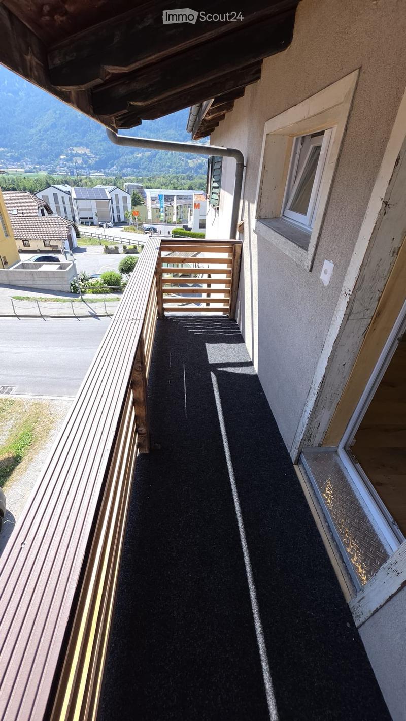 Balcony with wooden railing, dark flooring, and a view of a town and mountains.