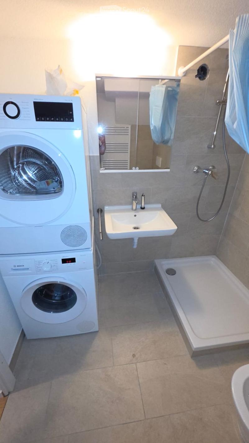 Modern bathroom with a washing machine, sink, bathtub, mirror, and shower area.