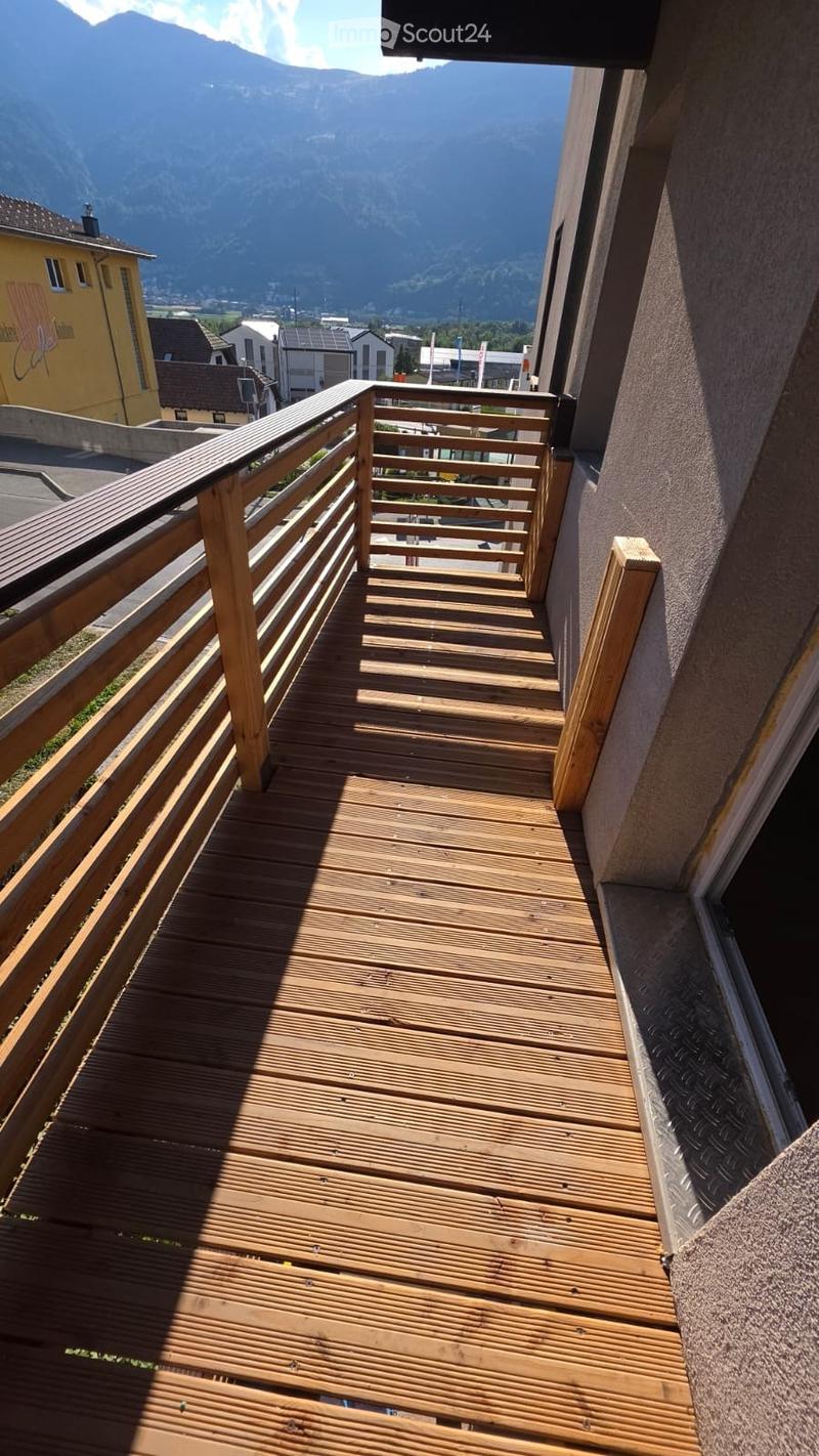 Wooden balcony with railing, overlooking a town and mountains.