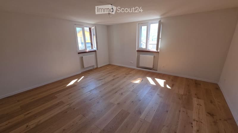 Empty room with wooden flooring, white walls, two windows, and radiators under each window.