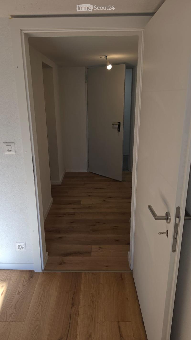 Empty hallway with wooden flooring, white walls, and a single open door leading to another room.