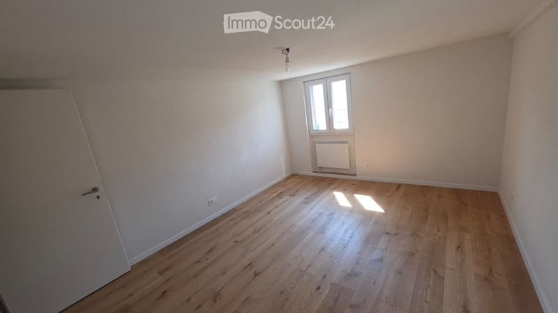 Empty room with wooden flooring, white walls, and a single window with a radiator below it.