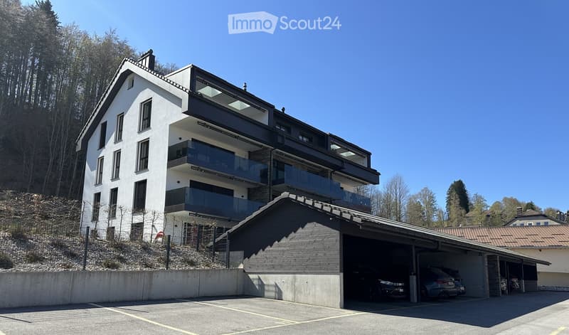 Modern multi-story building with balconies, garage, and parking area.