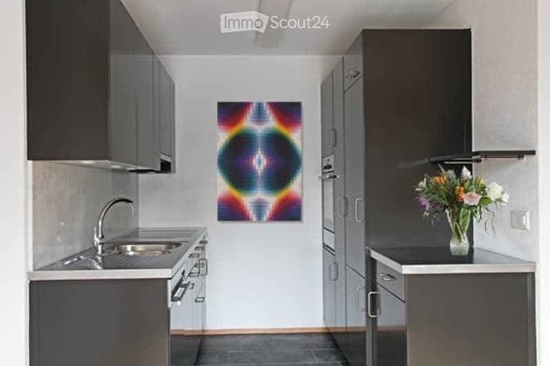 Modern kitchen with dark grey cabinets, stainless steel appliances, a sink with a faucet, a stove, and a colorful abstract painting on the wall. A vase with flowers sits on the counter.