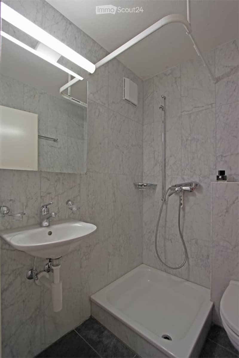 Modern bathroom with marble tiles, a white sink, a showerhead, a bathtub, and a toilet. The room features built-in lighting and a mirror above the sink.