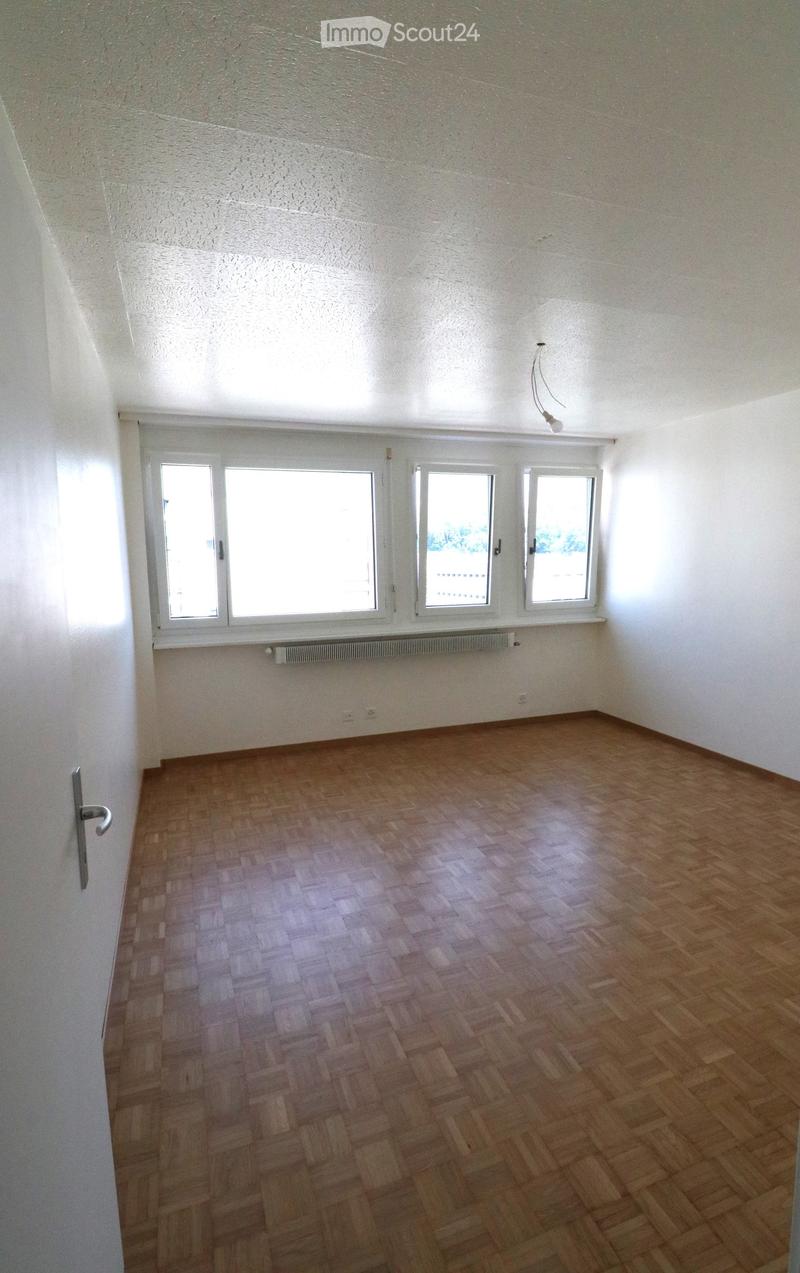 Empty room with wooden parquet flooring, white walls, and large windows allowing natural light. No furniture or equipment is present.