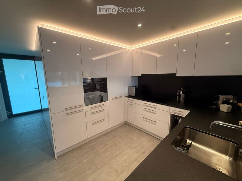 Modern kitchen with white cabinets, black countertops, stainless steel sink, and built-in lighting.