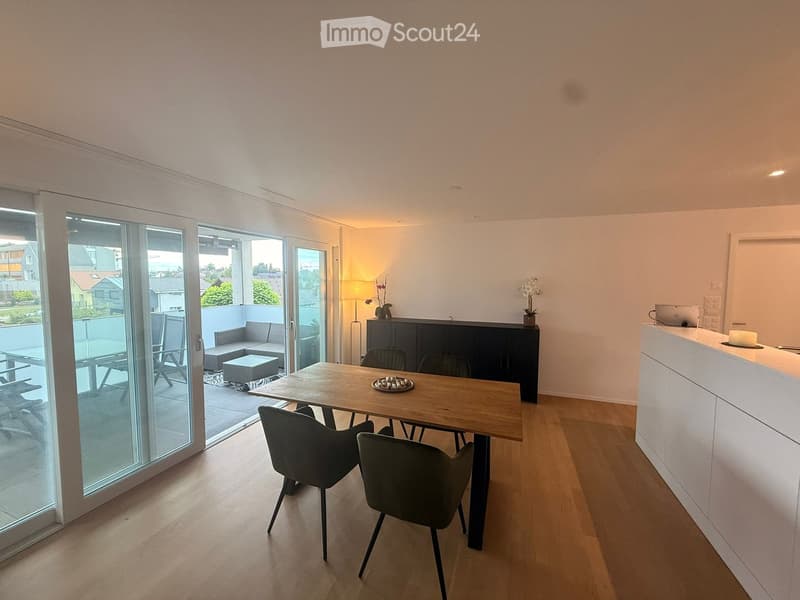 Bright, modern dining area with wooden floor, large sliding glass doors leading to a balcony, dining table with chairs, sofa, and a small cabinet.