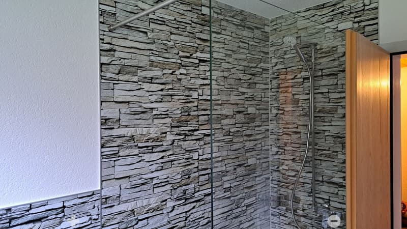 Modern bathroom shower area with stone tile walls, glass enclosure, and a handheld showerhead.