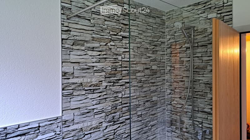 Modern bathroom shower area with stone tile walls, glass enclosure, and a handheld showerhead.