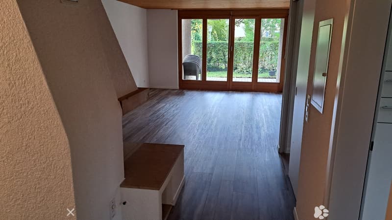 Empty hallway with wooden flooring, large glass doors leading to an outdoor area, and a small bench on the left side.
