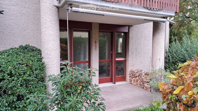 Entrance to a multi-story building with a covered walkway, glass doors, and surrounding greenery.