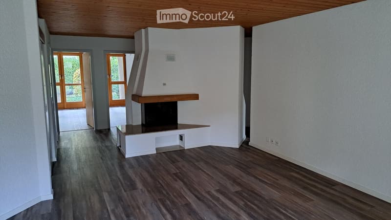 Empty living room with wooden flooring, white walls, and a built-in fireplace. Two large glass doors lead to an outdoor area.