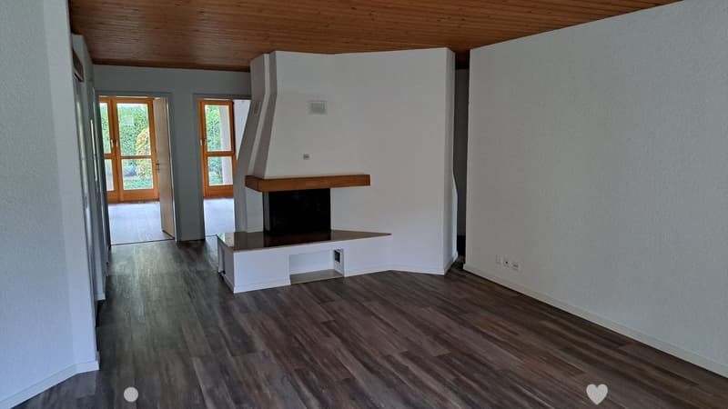 Empty living room with wooden flooring, white walls, and a built-in fireplace. Two large glass doors lead to an outdoor area.