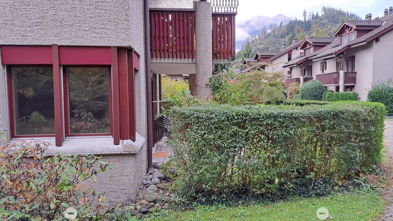 Modern multi-story building with large windows, red accents, and a well-maintained garden with shrubs and a stone pathway.
