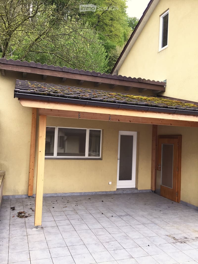 Balcony with tiled floor, wooden roof structure, and access doors to the house.