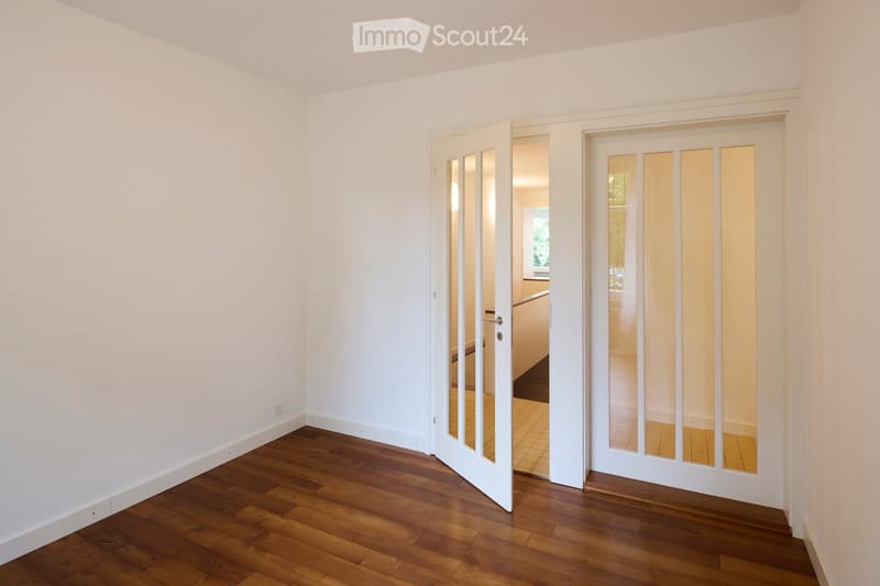 Empty hallway with wooden flooring, white walls, and two open doors leading to adjacent rooms.