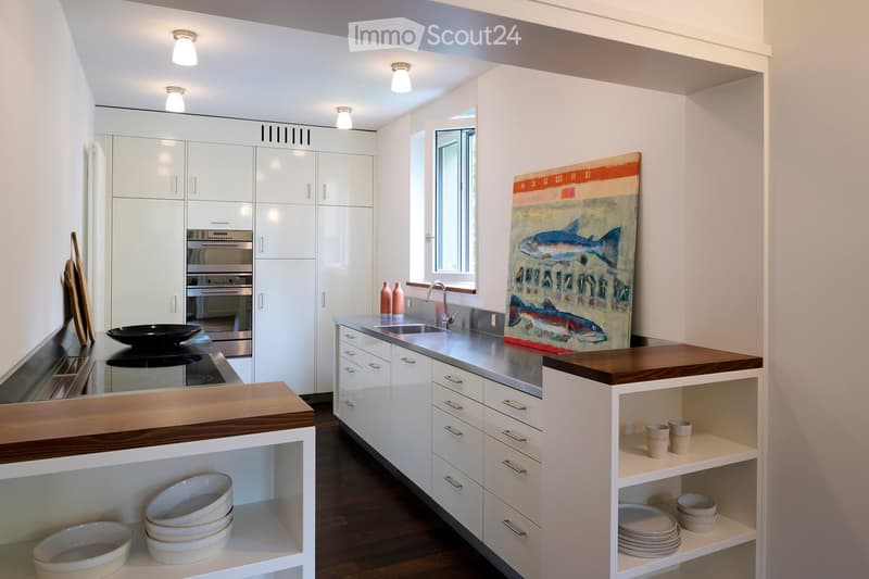 Modern kitchen with white cabinets, stainless steel appliances, wooden countertops, and a large window. Shelves hold bowls, plates, and cups.