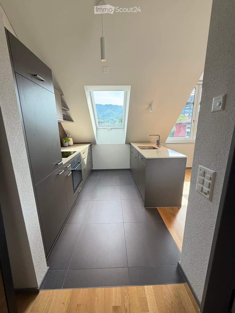 Modern kitchen with grey cabinets, dark tiled floor, and a central island with a sink and faucet. Features a skylight window and pendant light.