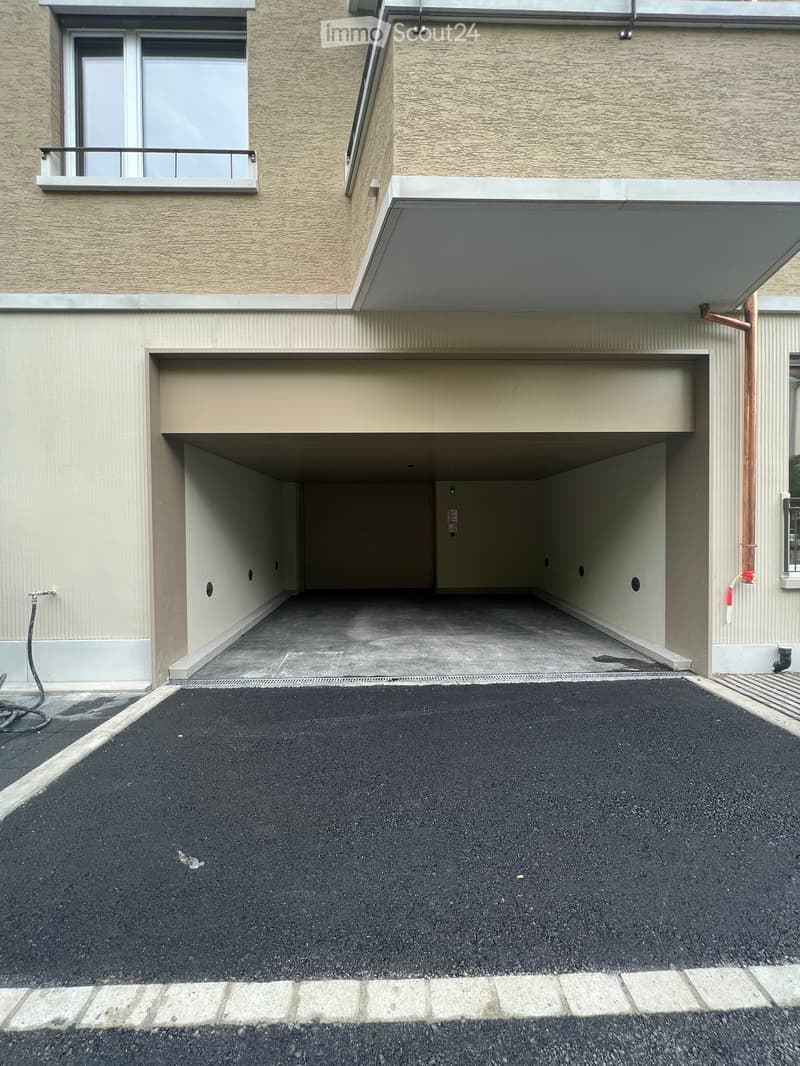 Modern building exterior with a covered garage entrance and a paved parking area.