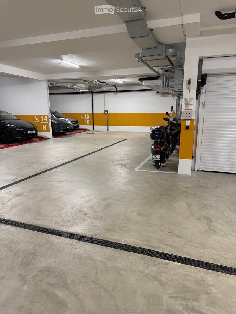 Underground parking area with concrete floor, white and yellow painted walls, two parked vehicles (car and motorcycle), and access doors.
