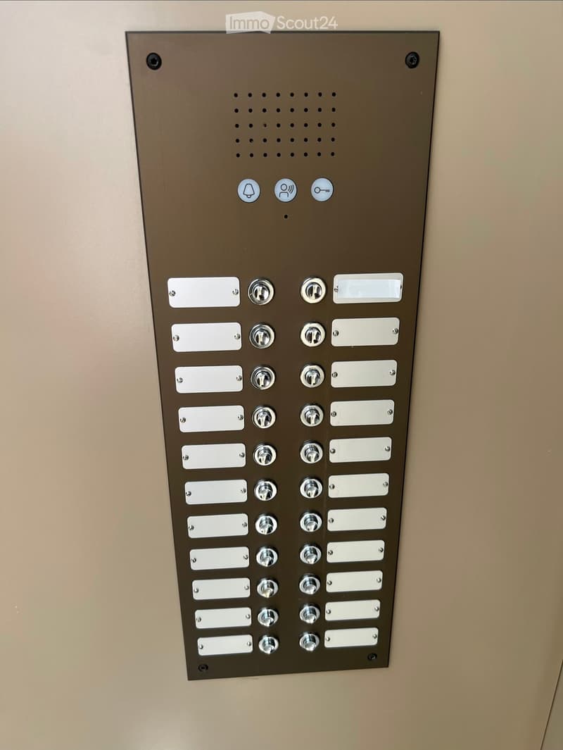A modern intercom panel with multiple call buttons and a small speaker icon, mounted on a beige wall.
