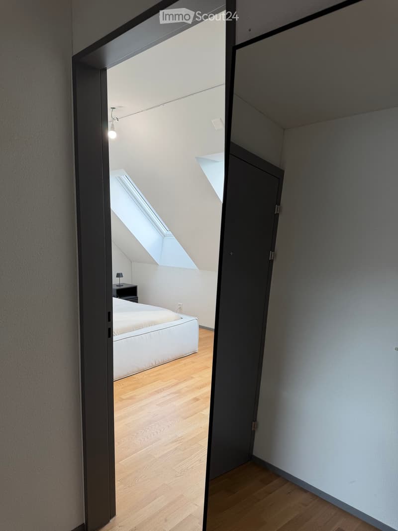 Modern bedroom with wooden flooring, white bed, nightstand, and a skylight window above the bed.