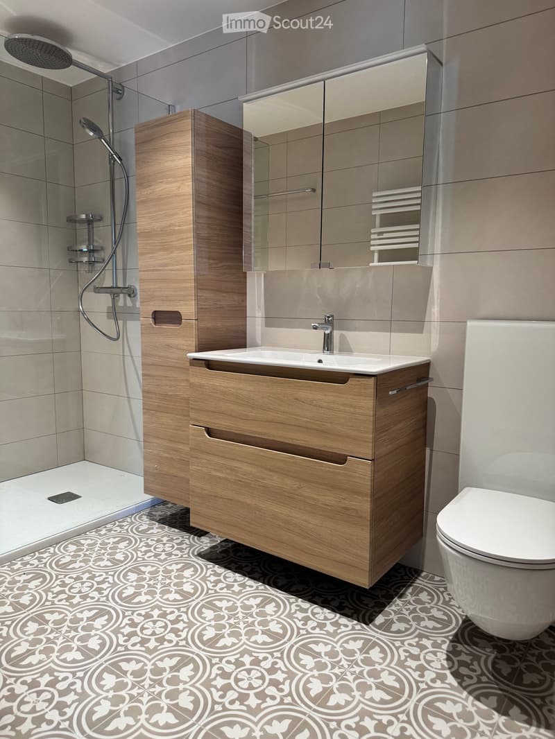 Modern bathroom with wooden vanity, sink, mirror, toilet, and shower area with glass enclosure.