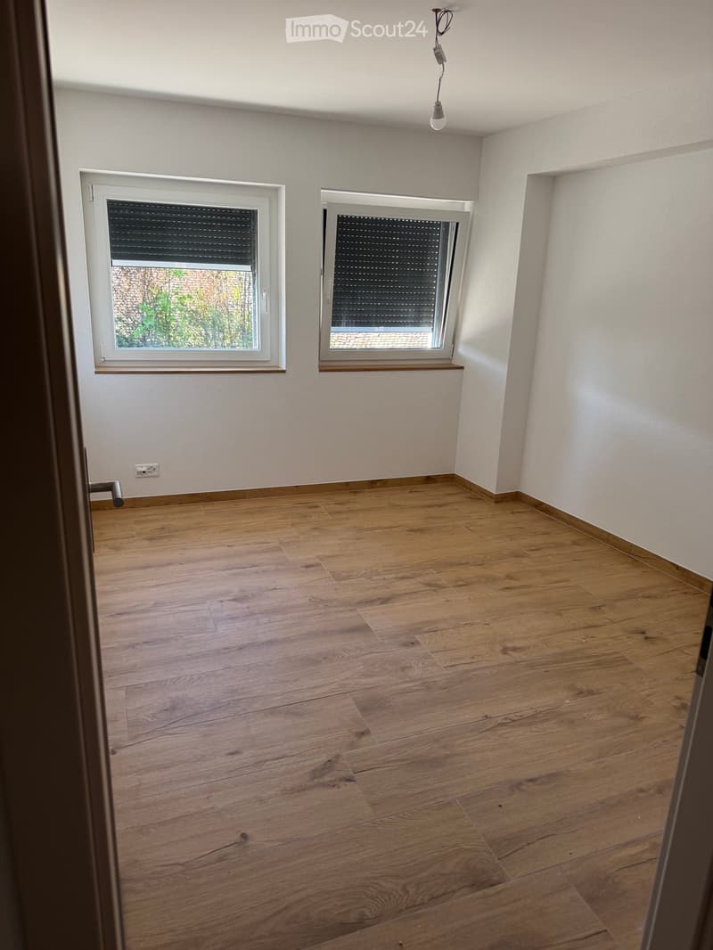 Empty room with wooden flooring, white walls, and two windows with blinds. No furniture or equipment present.