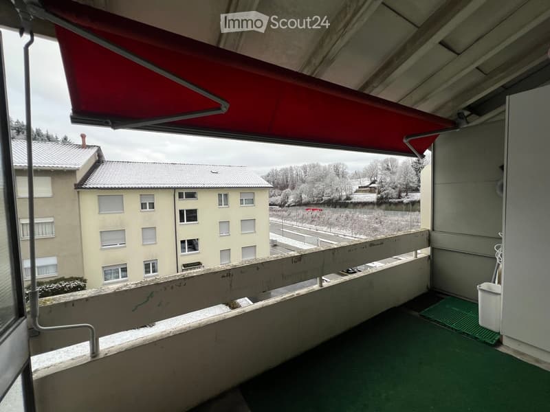Balcony with green flooring, red awning, and view of a residential building and snowy landscape.