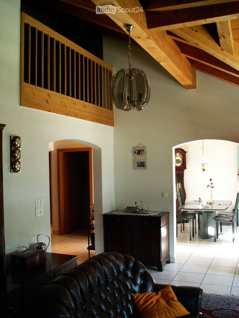 high ceiling with wooden beams, chandelier, sofa, dining table with chairs, grandfather clock, artwork on wall