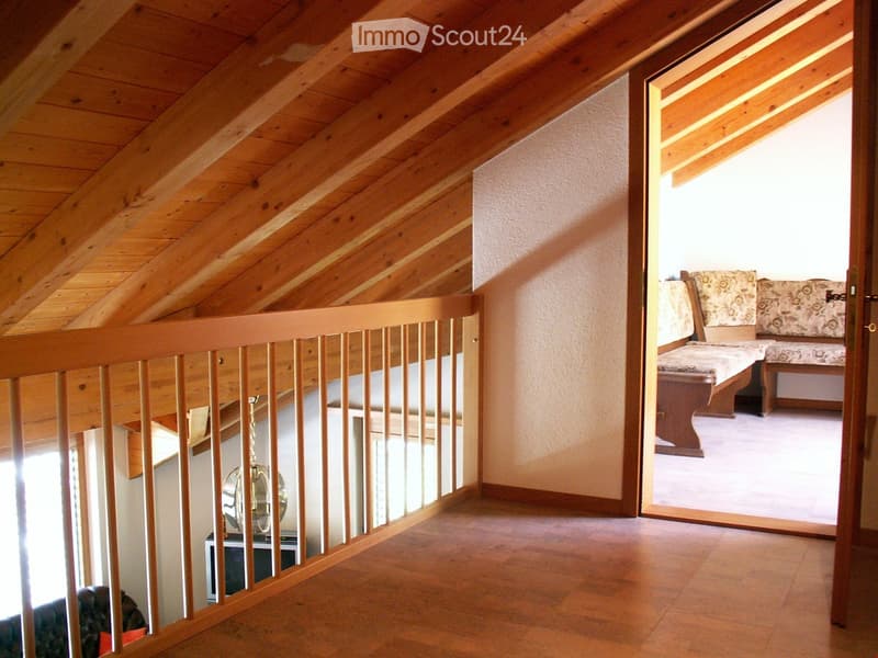 room with wooden balcony, exposed wooden ceiling, brown wood floor, white walls, open door, lounge area