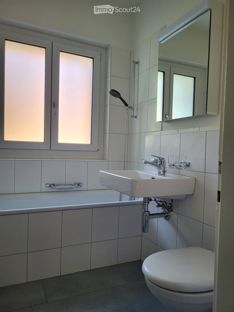Modern bathroom with white tiles, a sink, toilet, mirror, and showerhead.