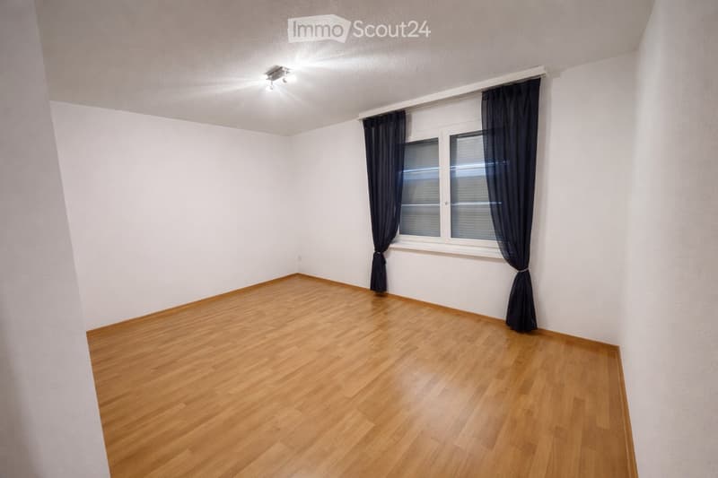 Empty room with wooden flooring, white walls, and a window with dark curtains.
