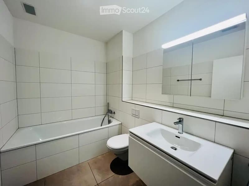 Modern bathroom with white tiles, a bathtub, toilet, sink, and a large mirrored cabinet.
