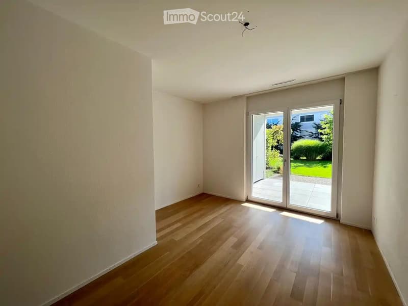 Empty room with wooden flooring, white walls, and large sliding glass doors leading to a patio area.