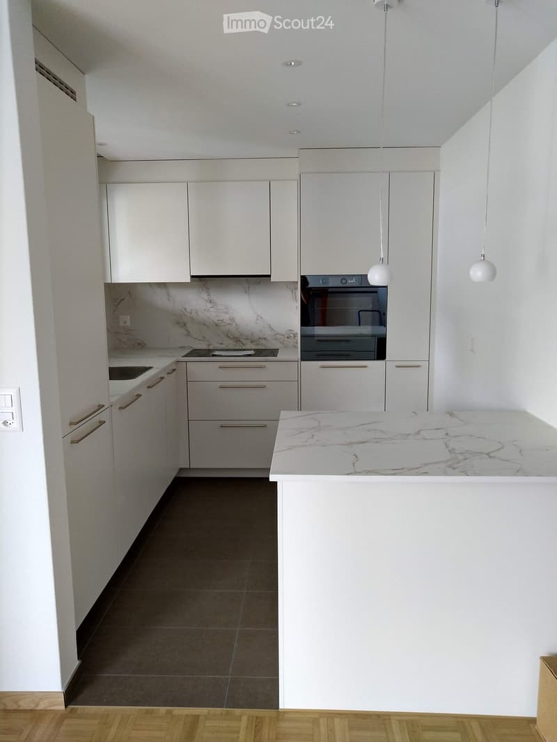 Modern kitchen with white cabinets, marble backsplash, island, and pendant lights.