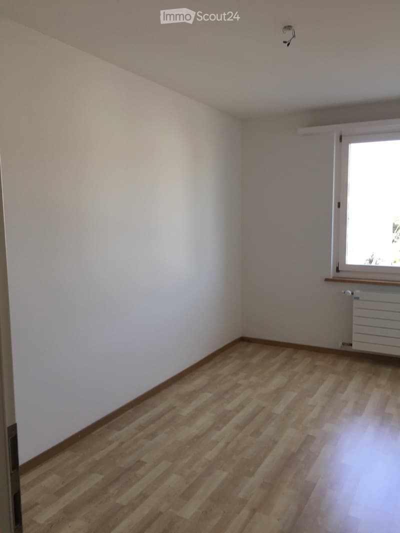 Empty room with light wooden flooring and white walls, featuring a window with a radiator below it.