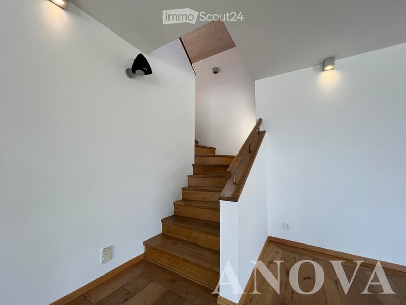 Wooden staircase with a wooden handrail, white walls, and modern wall-mounted lighting fixtures.