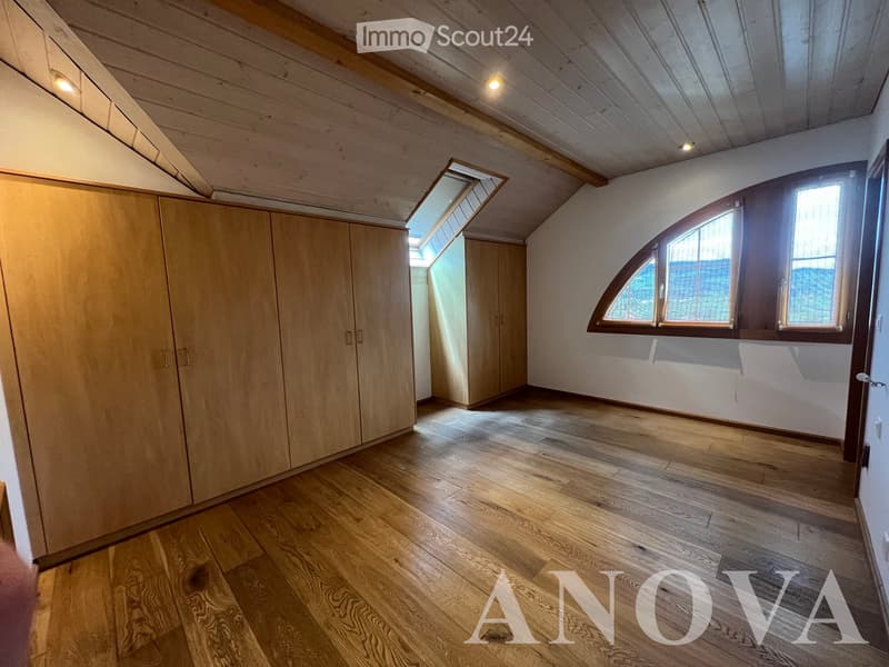 Empty attic room with wooden floors, exposed wooden beams, large windows, and a skylight, featuring built-in wooden wardrobes.