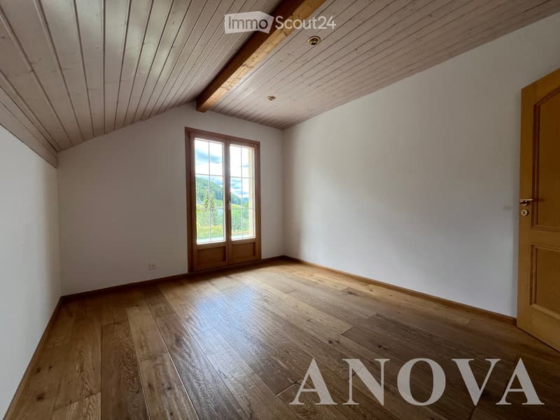 Empty room with wooden flooring, white walls, and a large window offering a scenic view. The ceiling features exposed wooden beams.