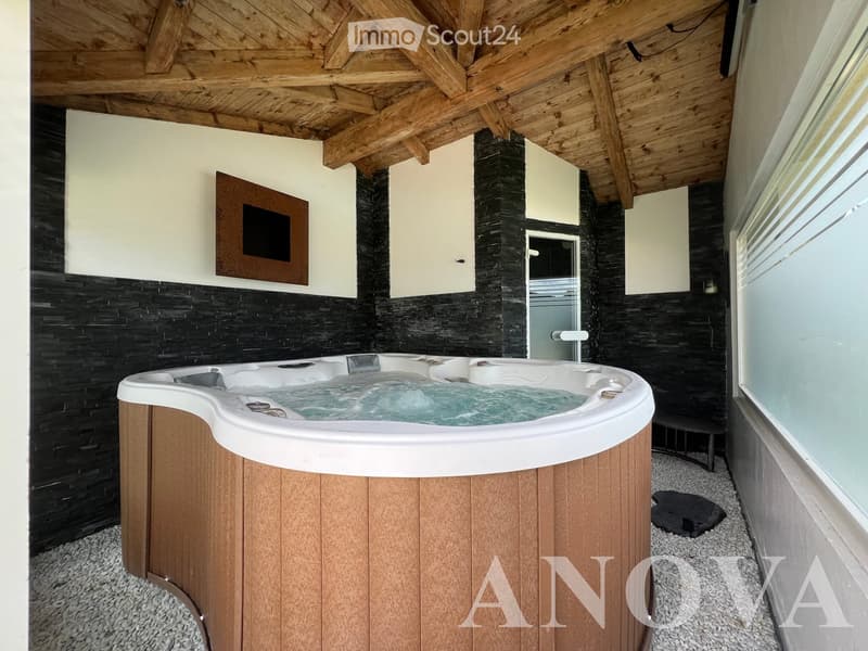 Modern bathroom with a wooden-framed bathtub, black tiled walls, and a wooden ceiling with exposed beams.