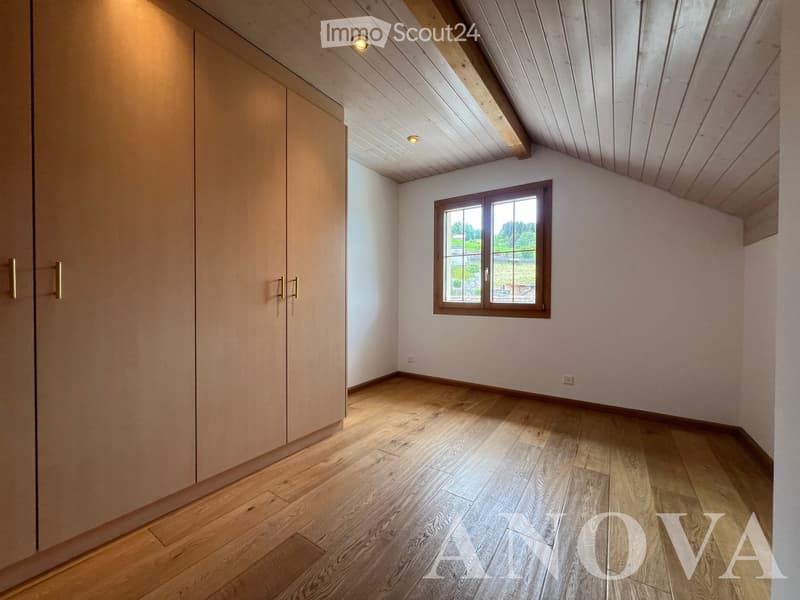 Empty room with wooden flooring, white walls, and a large window with wooden frame. The ceiling has exposed wooden beams and recessed lighting.