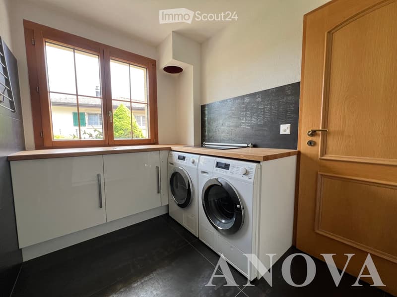 Modern bathroom with white cabinets, a washing machine, and a large window with wooden frames.