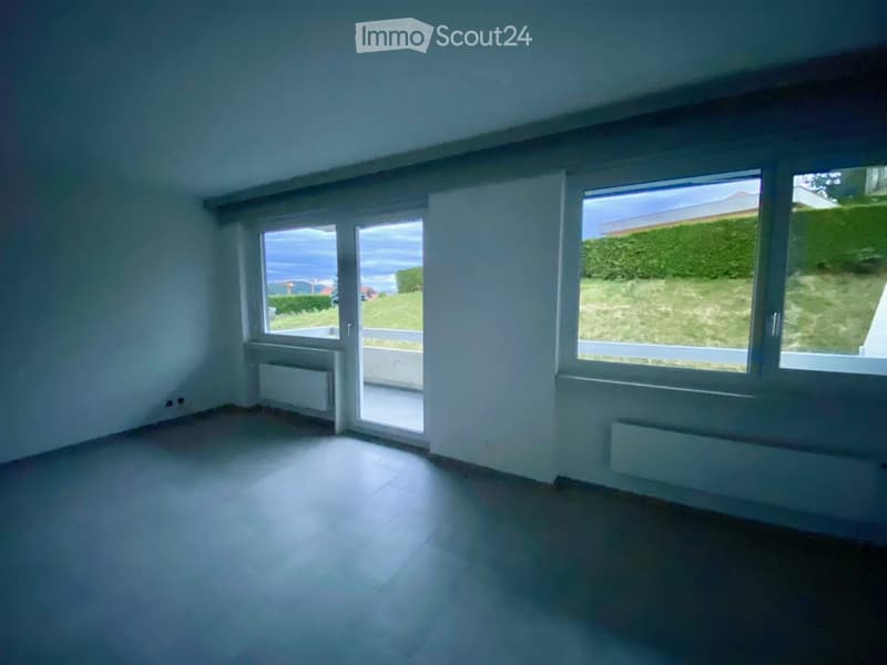 Empty room with tiled floor, white walls, large windows, and a sliding glass door leading to a balcony.